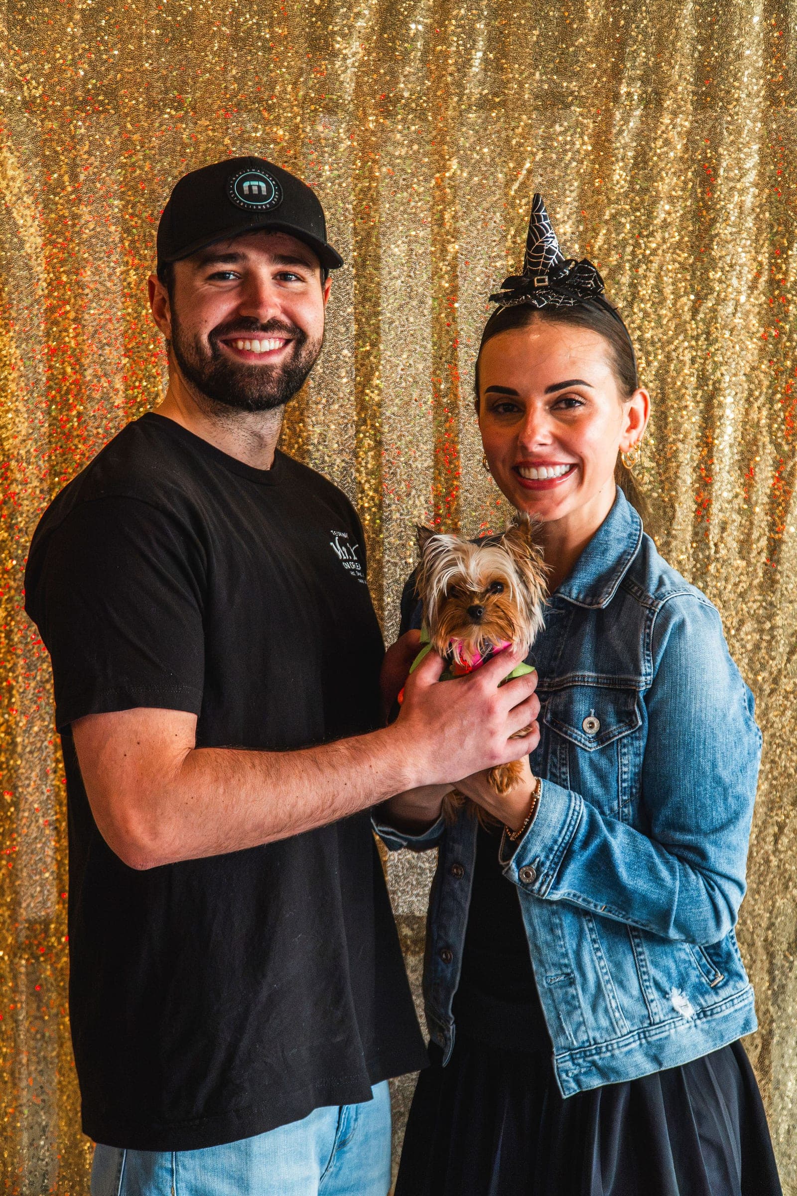 A couple photographed with their Yorkie against the gold sequin backdrop