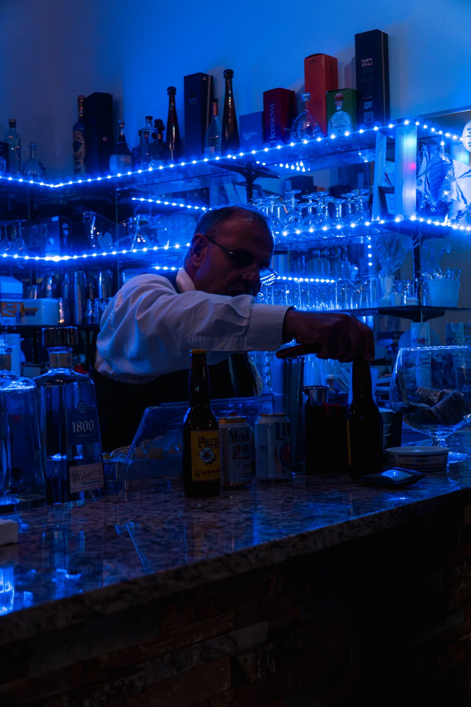 A bartender pouring drinks at a blue-lit bar during a celebration
