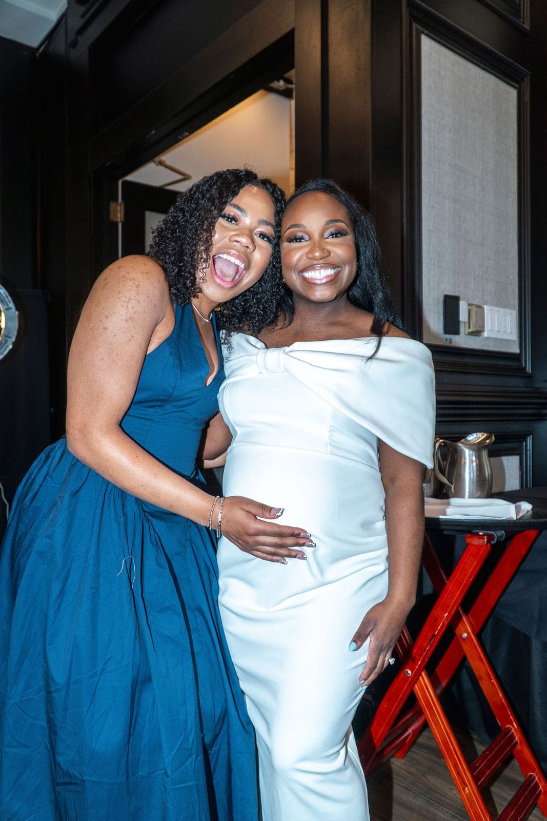 Two friends laughing together, one with a hand on the other's baby bump